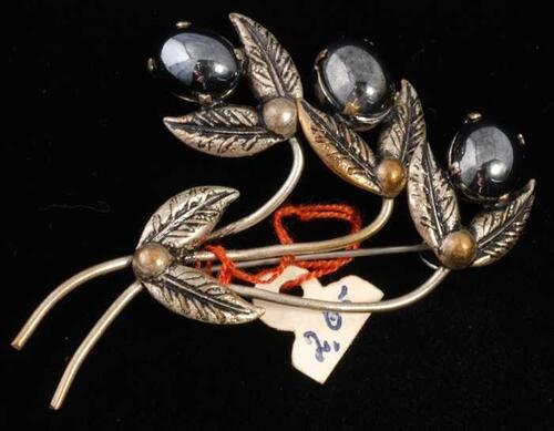 Broche, zilverkleurige metalen olijventakjes met blaadjes en gladde bolle zwarte stenen, kapper Van…