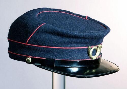 Donkerblauwe uniformpet van postbode met rode biezen en posthoorn