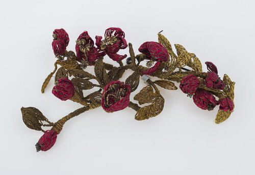Filligrain corsage van dun metaaldraad omwikkeld met gekleurd zijderaad, goudkleurig takje met rode…