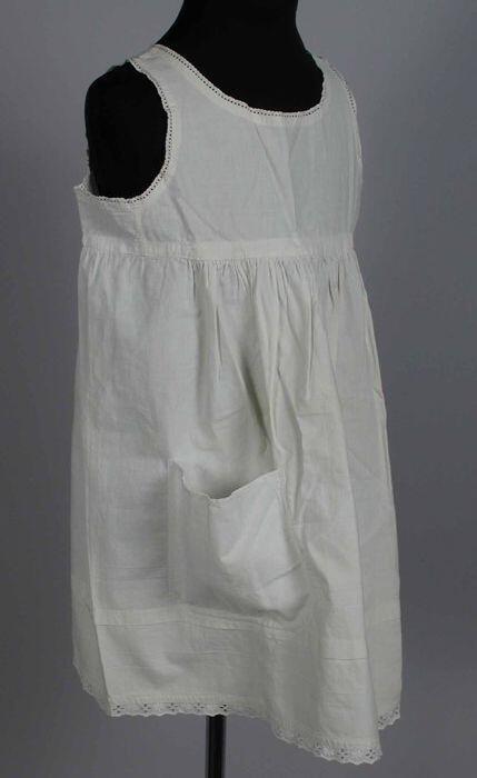 Kinderonderjurk, rechte pas met aangerimpeld rokdeel met grote (later) opgestikte zak, broderie…