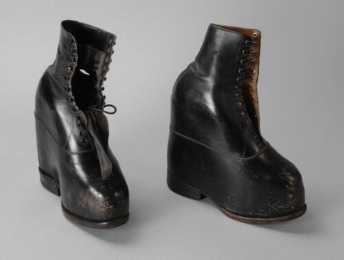 Twee orthopedische (linker-) schoenen van glad zwart leer met een zeer verhoogd voetbed, rijglaars…