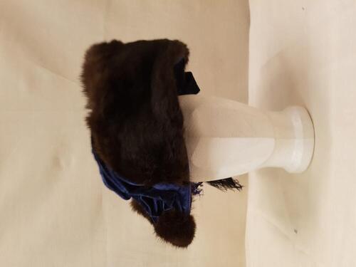 Hoed van helderblauw fluweel, gegarneerd met strook donkerbruin langharig bont en grote struisveren