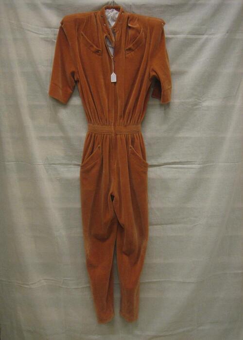 Jumpsuit van oranje-bruin fluweel, korte mouw, smalle pijpen en brede schouders