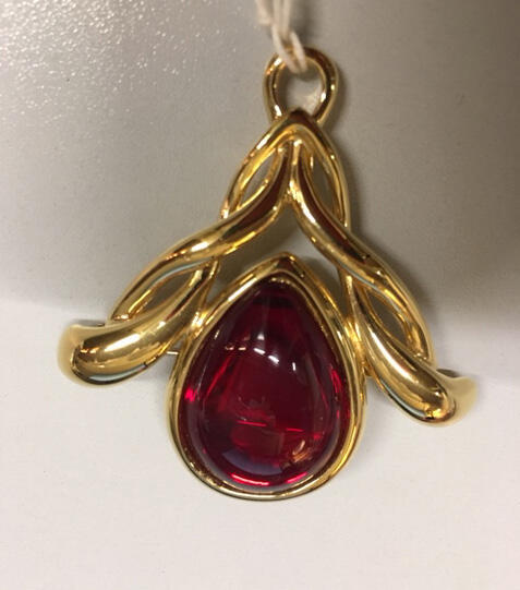 Broche met centraal een rood transparante druppelvorm in goudkleurig metaal gezet, behorende bij…