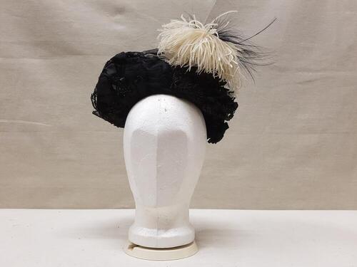 Dameshoed, toque, zwart gaas, rozetten van zwart satijn, repen zwart stro en broche van zwart glas…