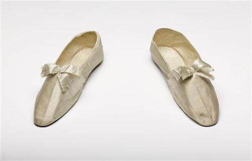 Schoentjes van wit satijn, op de voorschoen een strik van wit satijnlint. Geheel platte schoenen…