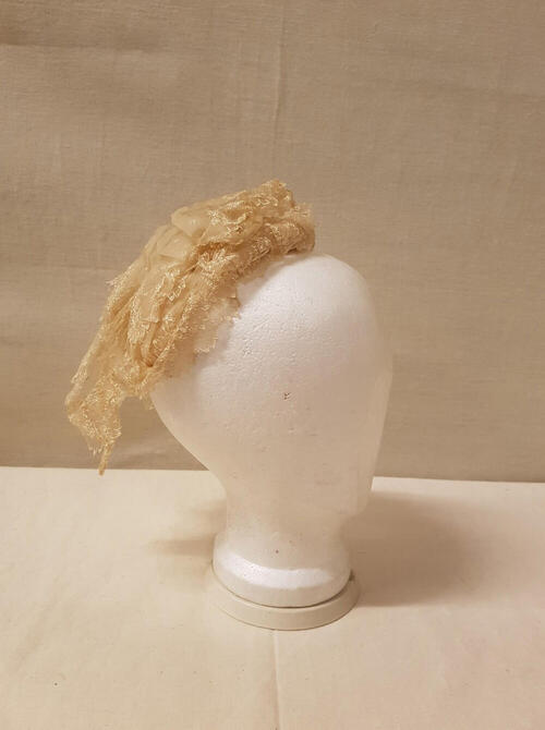 Coiffure / Kap bestaande uit stroken crèmekleurige effen organdie, machinaal geborduurd met…