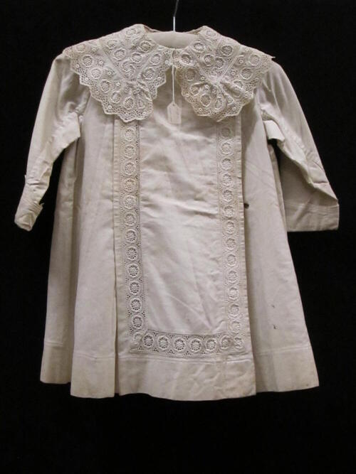 Jas (kind) van wit keperkatoen, geruwd aan de binnenzijde. Tussenzetsels van machinale broderie