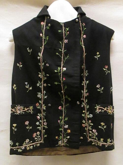 Vest (man) van zwart laken met randborduursel van veelkleurige bloemenslingers en strooimotief,…