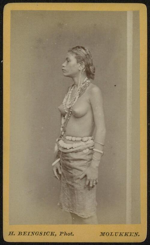 Portret van een staande Molukse vrouw met sarong en diverse sieraden