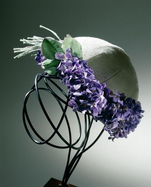 Muts van crèmekleurige wollen tricot versierd met een corsage en een rand van 'violettes de Parme'